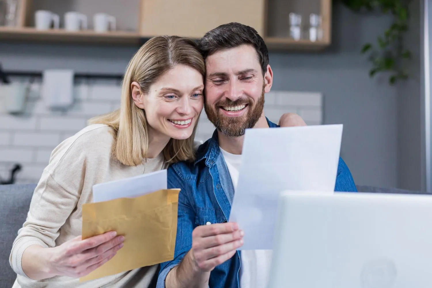 Smiling couple holding tax documents and an envelope beside a laptop.