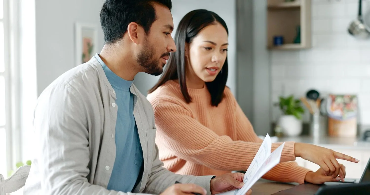 Couple reviewing paperwork together at a kitchen counter.