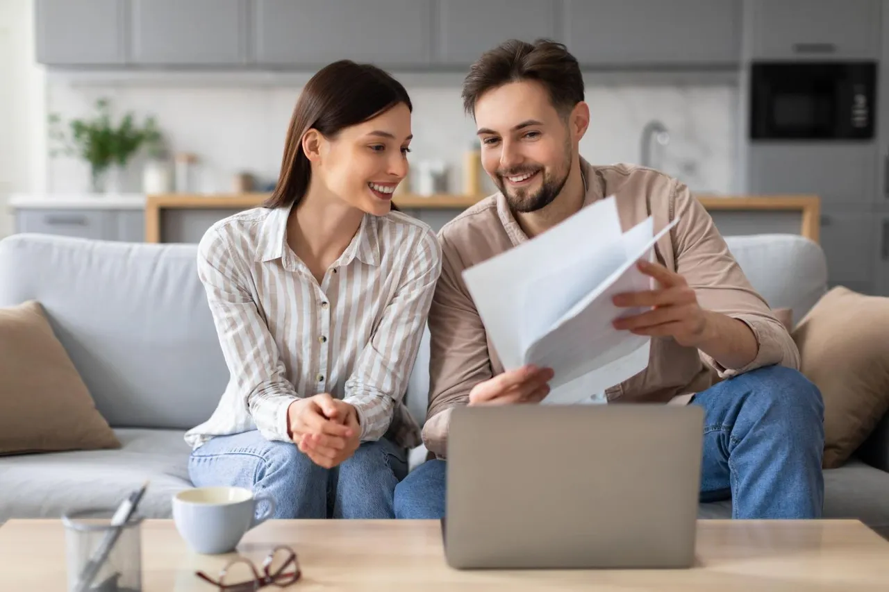 Couple on a sofa reviewing documents in front of a laptop.