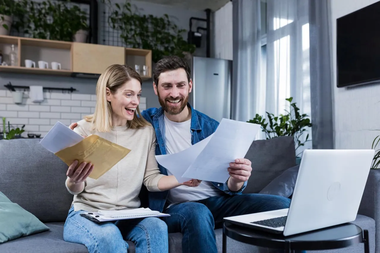 Couple on a sofa reviewing documents with a laptop on the table.
